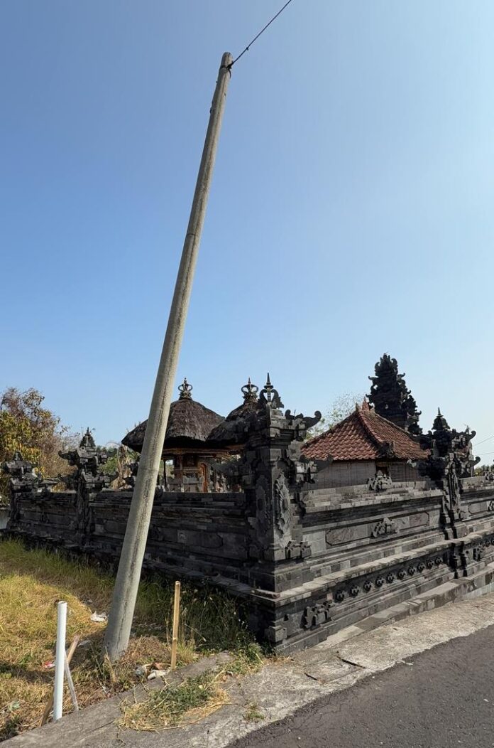 Tiang listrik PLN miring dekat Pura Dalem Bebali Kelod di Desa Berembeng, Selemadeg, Tabanan.